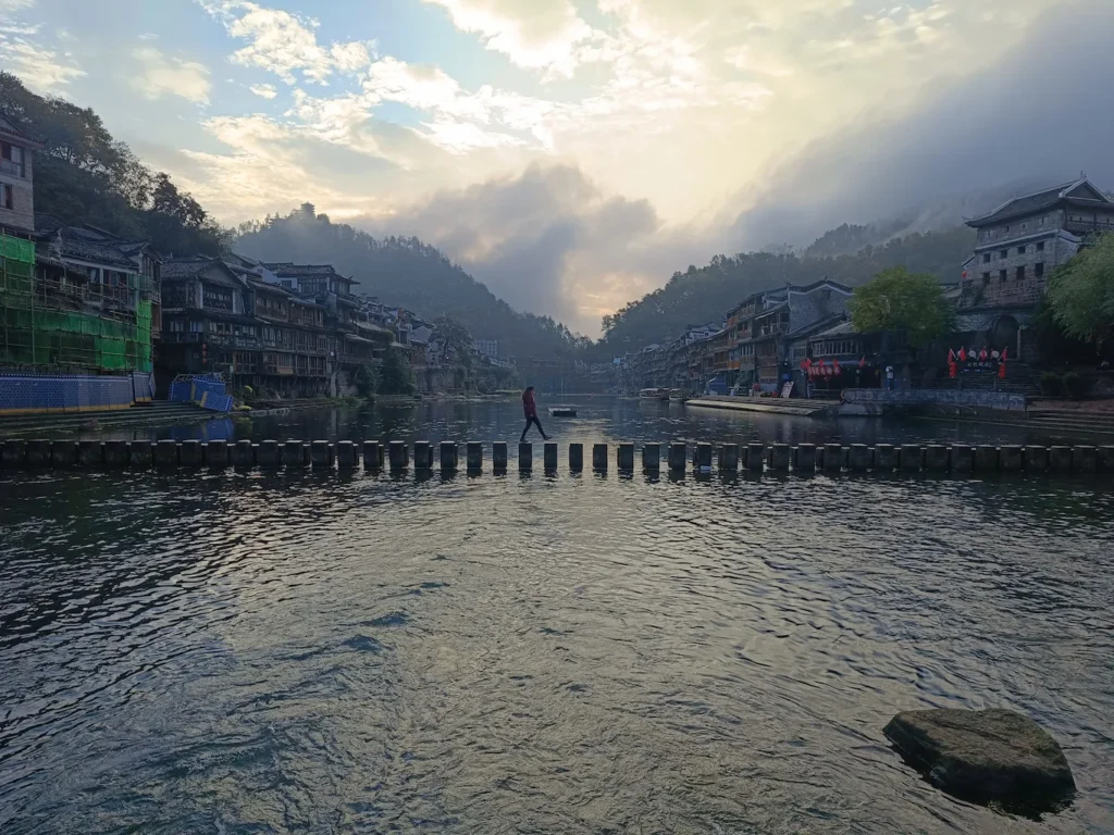 Chica cruzando el puente de piedras al amanecer en Fenghuang (China)